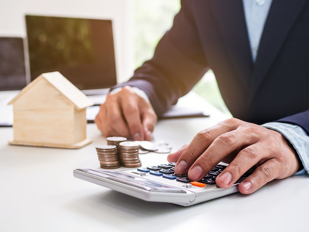 Immobilienbewertung berechnen – Wertermittlung mit Erfahrung Hände mit Taschenrechner, Münzen und Modellhaus auf dem Schreibtisch zur Immobilienbewertung