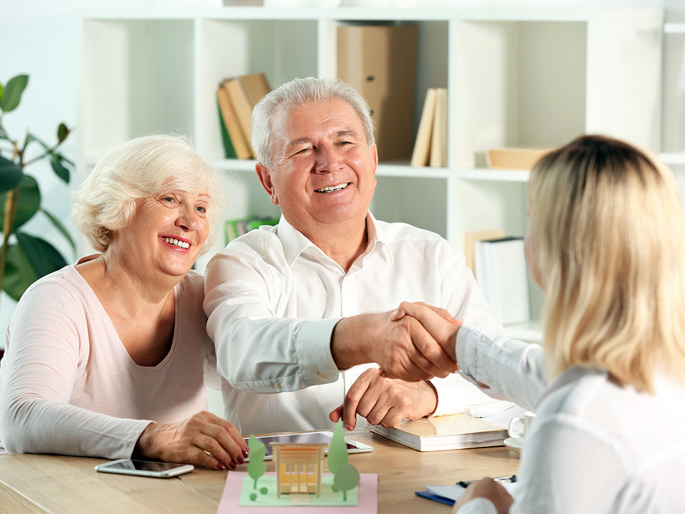 Immobilienverkauf & Beratung – sicher bis zum Notartermin Älteres Paar schüttelt einer Beraterin die Hand bei einem Termin rund um Immobilien